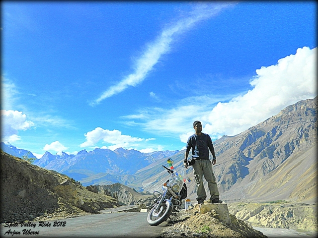arjun posing next to his bike with massive mountains